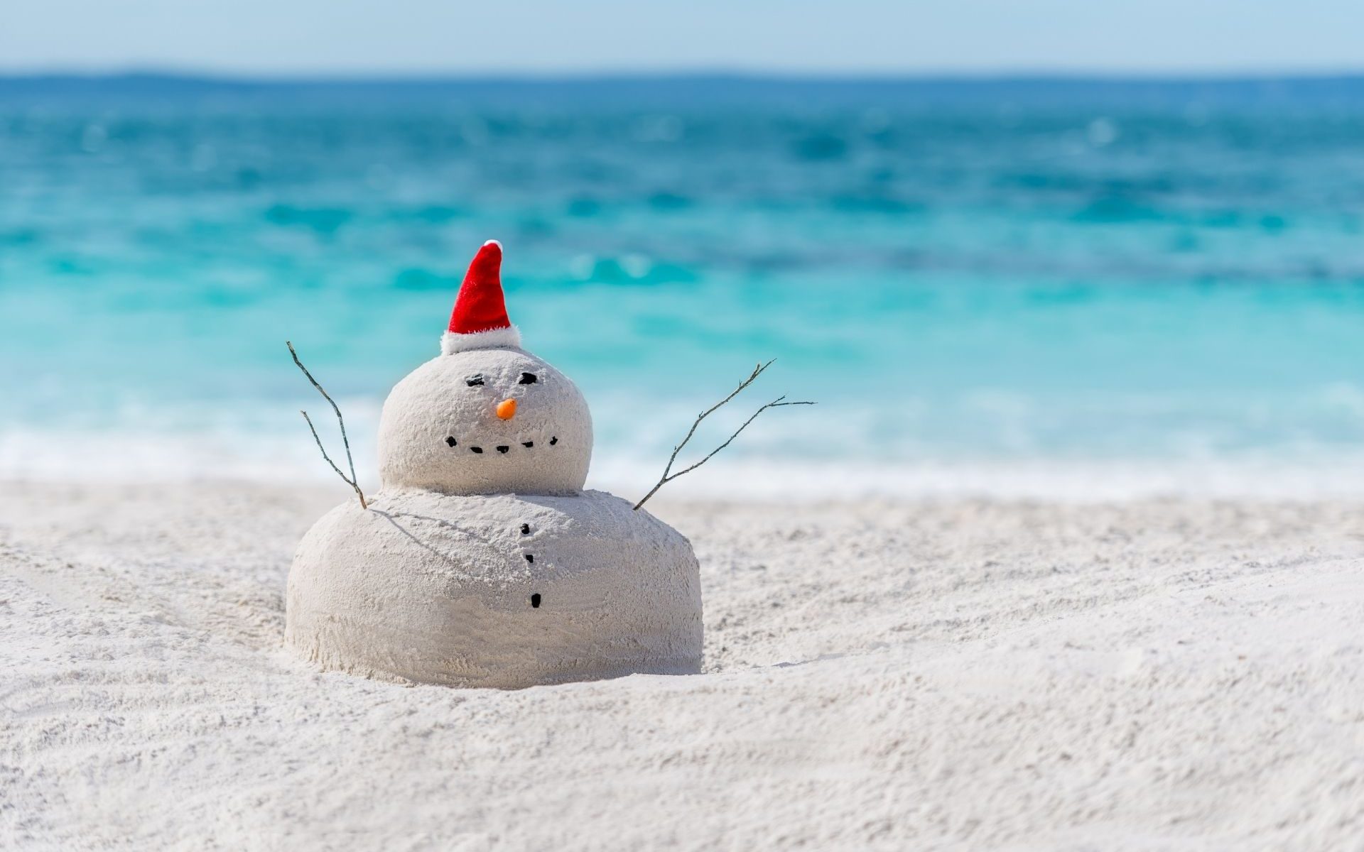 Snowman made from sand in a santa hat on the beach